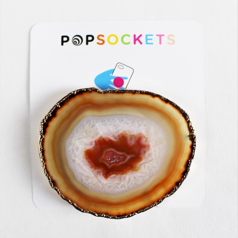 May include: A round, brown and white agate phone grip with a gold trim. The grip is designed to look like a slice of agate.