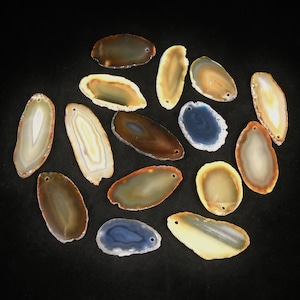 May include: Assortment of 14 agate slices in various colors and patterns, including brown, white, yellow, blue, and gray. The slices are oval-shaped and have a smooth, polished surface.