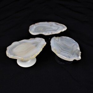 May include: Three white agate slices with natural patterns, each mounted on a phone grip stand.