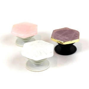 May include: Three phone grips with hexagonal tops. One is pink, one is white, and one is purple with a gold trim.