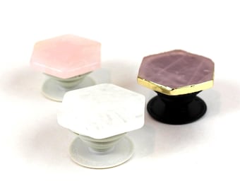 May include: Three phone grips with hexagonal tops. One is pink, one is white, and one is purple with a gold trim.
