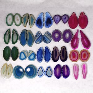 May include: Assortment of agate slices in various colors, including blue, green, purple, pink, and white. The slices are arranged in pairs and are approximately 2 inches in diameter.