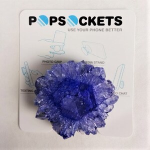 May include: A purple crystal-shaped phone grip with the text "PopSockets Use Your Phone Better" on a white background.