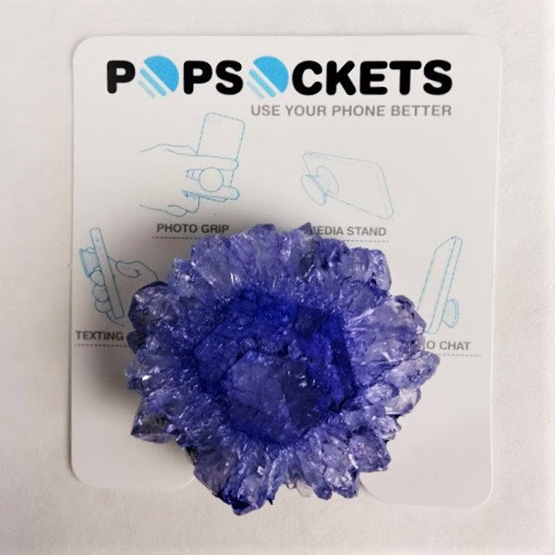 May include: A purple crystal-shaped phone grip with the text "PopSockets Use Your Phone Better" on a white background.