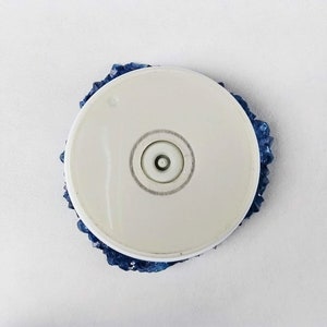 May include: A white round base with a blue crystal-like design around the edge. The base has a small round hole in the center.