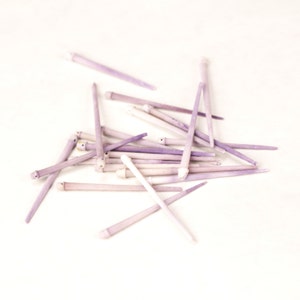 May include: A pile of approximately 20 purple and white slender sticks, possibly made of wood or bone, on a white background.