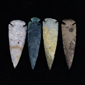 May include: Four arrowheads made of different types of stone. The arrowheads are all pointed and have a variety of colors and patterns.