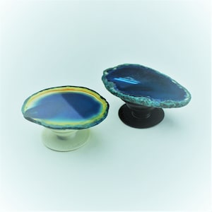 May include: Two agate phone grips, one with a blue and green agate slice on a black base and the other with a blue, green, and yellow agate slice on a white base.