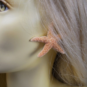 May include: A close-up of a person's ear with a light orange starfish earring. The starfish is a natural sea creature and has a rough texture.