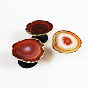 May include: Three agate phone grips with gold trim. The agate is a reddish-brown color with white and orange banding.