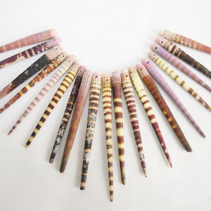 May include: A collection of 15 small, pointed seashells with brown, white, and pink stripes. The shells are arranged in a semi-circle on a white background.
