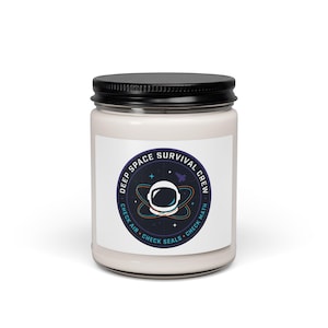 May include: A white candle in a glass jar with a black lid. The label reads "DEEP SPACE SURVIVAL CREW" with an astronaut helmet graphic and the phrases "CHECK AIR, CHECK SEALS, CHECK MATH."