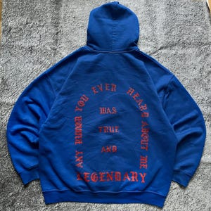 May include: A royal blue hoodie with a hood and long sleeves. The back of the hoodie features the text "ANY RUMOR YOU EVER HEARD ABOUT ME WAS TRUE AND LEGENDARY" in a red, gothic-style font.