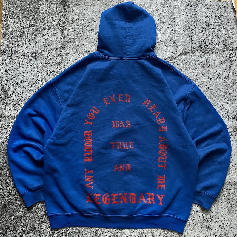 May include: A royal blue hoodie with a hood and long sleeves. The back of the hoodie features the text "ANY RUMOR YOU EVER HEARD ABOUT ME WAS TRUE AND LEGENDARY" in a red, gothic-style font.