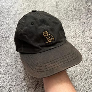 Puede incluir: Gorra de b&eacute;isbol negra con visera curva. La gorra presenta un logotipo de b&uacute;ho bordado en dorado en la parte delantera. Hecha de tela duradera, tiene un bot&oacute;n en la parte superior. Un estilo cl&aacute;sico.