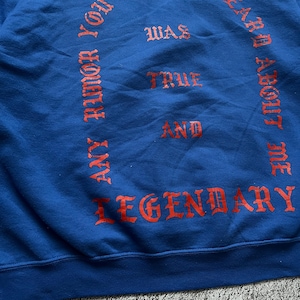 May include: A blue sweatshirt with red lettering. The text includes the phrases "ANY RUMOR YOU HEARD ABOUT ME WAS TRUE AND LEGENDARY". The sweatshirt is made of a soft material.