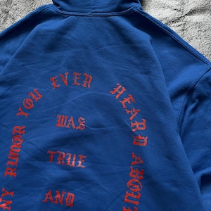 May include: A blue hoodie with red text that reads "ANY RUMOR YOU EVER HEARD ABOUT WAS TRUE AND". The hoodie has a hood and is made of a soft material. The text is in a gothic font.