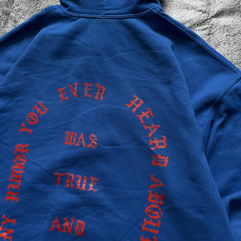 May include: A blue hoodie with red text that reads "ANY RUMOR YOU EVER HEARD ABOUT WAS TRUE AND". The hoodie has a hood and is made of a soft material. The text is in a gothic font.