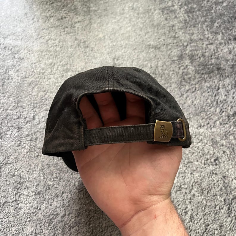 Puede incluir: Gorra de b&eacute;isbol negra con visera curva y correa ajustable. La gorra presenta una hebilla de metal color bronce con un emblema de b&uacute;ho. La gorra est&aacute; hecha de una tela desgastada y texturizada.
