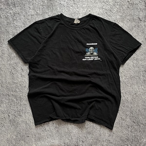 May include: A black short-sleeved t-shirt featuring a small graphic on the upper left chest. The graphic displays a black and white portrait of a person with blue rain-like streaks above them, accompanied by the text KASABIAN FOR CRYING OUT LOUD (2017).
