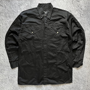 Può includere: Una camicia nera a maniche lunghe con abbottonatura, colletto a punta, due tasche sul petto con patte a punta e bottoni a pressione in metallo dorato. La camicia presenta un'etichetta del marchio visibile all'interno del colletto e polsini.