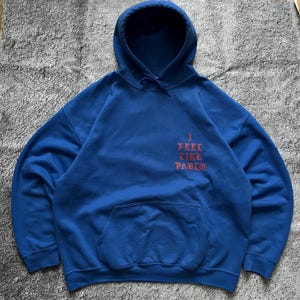 May include: A blue hooded sweatshirt with a front pocket and drawstring. The text "3 FEEL LIKE PABLO" is printed in red on the front. The sweatshirt has a lined hood.