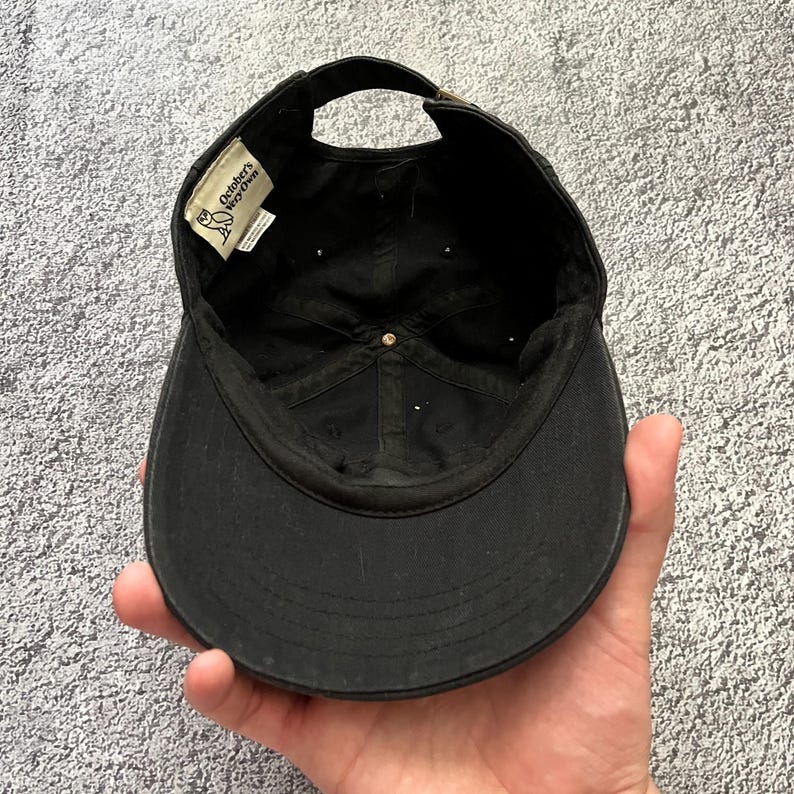 Puede incluir: Gorra de b&eacute;isbol negra con visera curva y correa ajustable. El interior presenta una etiqueta con el texto "October's Very Own" y un logotipo. La gorra est&aacute; hecha de tela duradera y tiene un estilo cl&aacute;sico e informal.