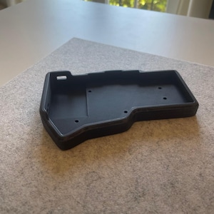 Peut inclure: Un étui noir rectangulaire imprimé en 3D avec une surface texturée. Le boîtier a une forme profilée avec plusieurs petits trous et une découpe rectangulaire. Le boîtier est conçu pour contenir un appareil.