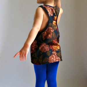 Puede incluir: Una persona joven lleva una camiseta sin mangas de estampado floral sobre fondo negro y leggings azules. La camiseta tiene un escote redondo y un estilo de espalda nadadora.