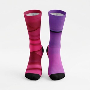 May include: A pair of crew socks with a vibrant color scheme. One sock features shades of pink and red in a layered design, while the other transitions from purple to pink. Both socks have black toes and the word "AURA" printed on the top.