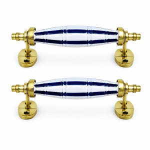 Può includere: Due maniglie per armadietto con un elemento centrale cilindrico in ceramica a righe orizzontali blu navy e bianche. Le maniglie sono supportate da finiture in metallo color oro lucido, incluse piastre di montaggio ovali con due fori ciascuna.