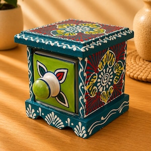 May include: A small square wooden storage box with a single drawer, painted in teal with intricate red, yellow, and white floral patterns. The drawer front is bright lime green with a white and blue floral design and a round, light green knob.