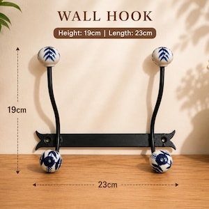 May include: A black metal wall hook with four white ceramic knobs featuring blue floral patterns. The hook has a height of 19 cm and a length of 23 cm, as indicated by the text labels. The design includes two vertical bars with rounded ends.