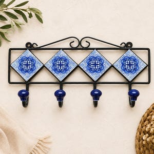 May include: A wall-mounted coat rack featuring a black metal frame with four diamond-shaped ceramic tiles. Each tile displays a blue and white floral pattern. Four matching blue ceramic knobs are attached to the bottom of the metal frame.