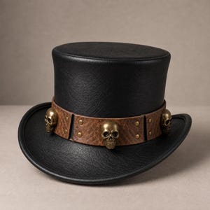 May include: A black top hat with a textured finish featuring a brown leather-like band around the base. The band is decorated with three metallic brass-colored skull ornaments and small circular studs, creating a distinct contrast against the black.