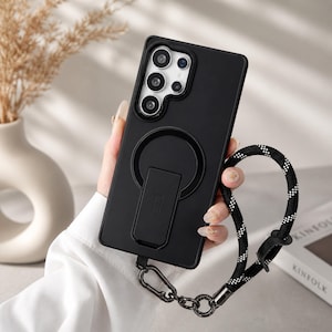 Może przedstawiać: Czarny futerał na telefon z wbudowaną podstawką i czarno-białą smyczą. Etui posiada okrągłe mocowanie magnetyczne i metalowy zatrzask. Etui na telefon ma chronić telefon i umożliwiać bezobsługowe oglądanie.