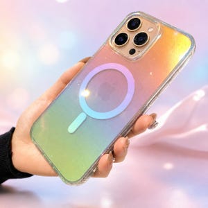 May include: A clear smartphone case with a glittery, iridescent gradient finish transitioning from orange to green. The case features a circular magnetic charging ring in the center with a light blue and pink hue, surrounding a visible Apple logo.