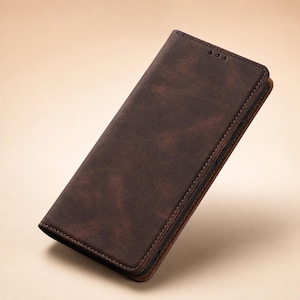 May include: A dark brown, rectangular wallet-style phone case with a textured, matte finish. The case features visible stitching along the edges and three small circular cutouts at the top of the front cover, designed to accommodate a speaker.