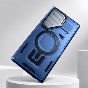 Op de afbeelding: Blauwe telefoonhoes met een geometrisch ontwerp. De hoes heeft een zilverkleurige metalen accent en een zwart cirkelvormig detail. De hoes is getextureerd en heeft een ingebouwde standaard.