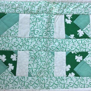 May include: A green and white patchwork quilt with a shamrock pattern. The quilt is made up of squares of different fabrics, including a green fabric with white shamrocks, a white fabric with green shamrocks, and a green and white checkered fabric.