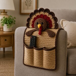 May include: A beige crochet armchair caddy featuring a turkey design with a brown, red, and tan fan-shaped tail, a brown head with black eyes, a yellow beak, and a red wattle. The caddy has three pockets and holds a black remote control.