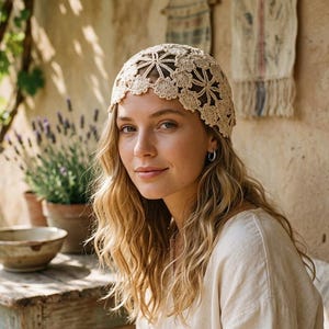 Könnte beinhalten: Eine beige Häkelkappe mit einem zarten Blumenmuster und komplexen Durchbruchdetails. Die Kopfbedeckung ist aus feinem Garn gefertigt und zeigt ein kreisförmiges Motiv an der Krone, das in gebogte Ränder übergeht und eine strukturierte Optik bietet.