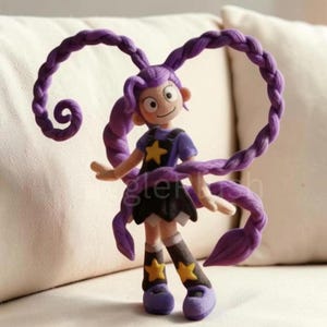 Puede incluir: Figura artesanal de un personaje de dibujos animados con pelo largo trenzado de color p&uacute;rpura. El personaje viste un top azul con una estrella amarilla, una falda negra y zapatos morados. La palabra "gler" es visible en la figura.