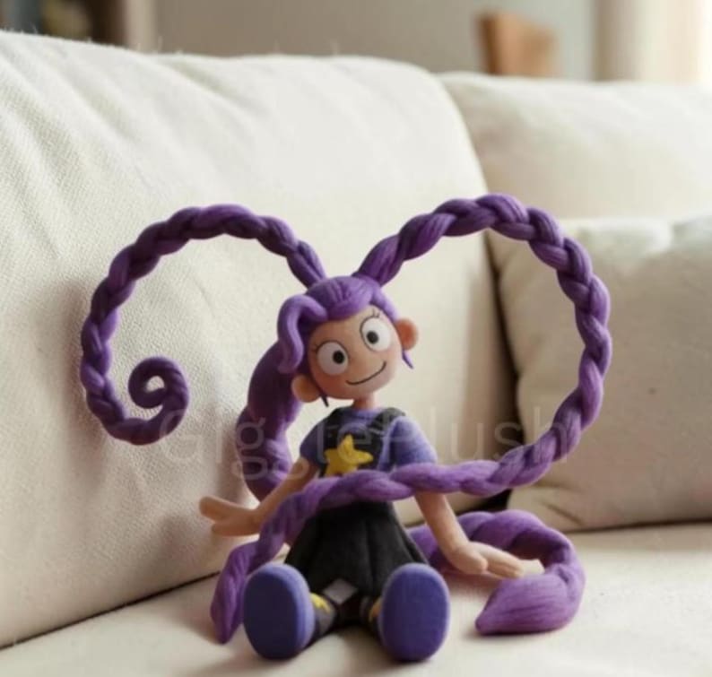 Puede incluir: Mu&ntilde;eca hecha a mano con cabello morado peinado en largas trenzas. La mu&ntilde;eca lleva una camisa morada con una estrella amarilla y una falda negra. La mu&ntilde;eca est&aacute; sentada en un sof&aacute; blanco.