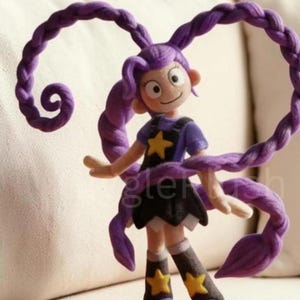 Puede incluir: Mu&ntilde;eca hecha a mano con largo cabello trenzado morado. La mu&ntilde;eca viste una camiseta morada con una estrella amarilla, una falda negra y botas moradas con estrellas amarillas. Los brazos de la mu&ntilde;eca est&aacute;n extendidos y tiene una expresi&oacute;n sonriente.