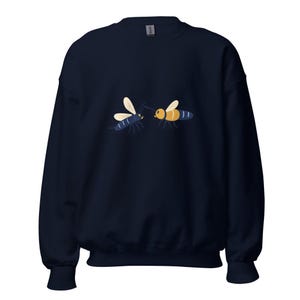 Può includere: Una felpa girocollo blu navy con un'illustrazione grafica di due api che si fronteggiano. Un'ape è prevalentemente blu scuro con ali chiare, mentre l'altra è gialla e blu scuro con ali chiare. Il disegno è posizionato al centro del petto.
