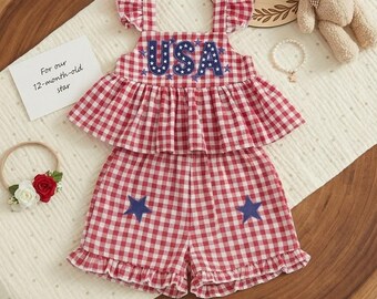 May include: A red and white gingham two-piece outfit featuring a sleeveless top with ruffled straps and a ruffled bodice, and matching shorts with ruffled hems. The top displays the text USA in blue with white stars, and the shorts feature blue stars.