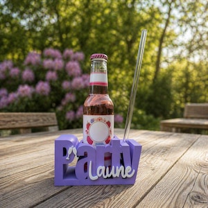 Puede incluir: Un soporte para bebidas morado con la palabra "Party" y el nombre "Laune" en blanco. Una botella de bebida rosa y una pajita transparente están en el soporte. La botella tiene una etiqueta blanca con un diseño de bayas. El soporte está sobre una mesa de madera.