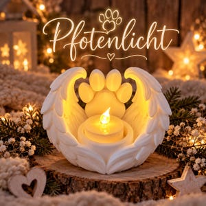 Peut inclure: Un bougeoir blanc avec un motif central en forme de patte encadré par deux ailes d'ange. Le support contient une petite bougie LED lumineuse. Au-dessus de l'objet, le texte Pfotenlicht est écrit en écriture cursive.
