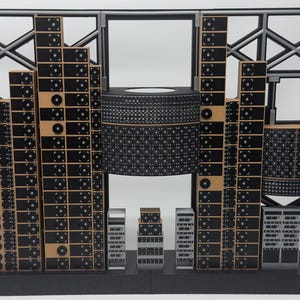 May include: A scale model of a server room featuring a black and gray lattice frame backdrop. The structure includes multiple vertical towers of black server racks with circular fan details, a large central cylindrical unit, and smaller rack components.